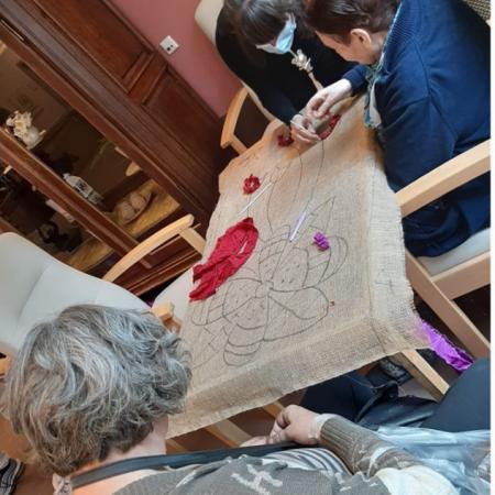 2 oude en 1 jonge vrouw werken aan een borduurwerk met bloemafbeelding