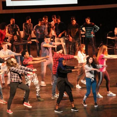 een diverse groep van een 25-tal jongeren danst synchroon op een podium