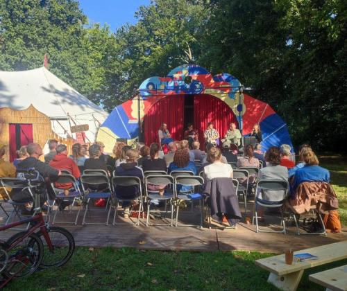 zicht op zittend publiek en buitenpodium, en een circustent